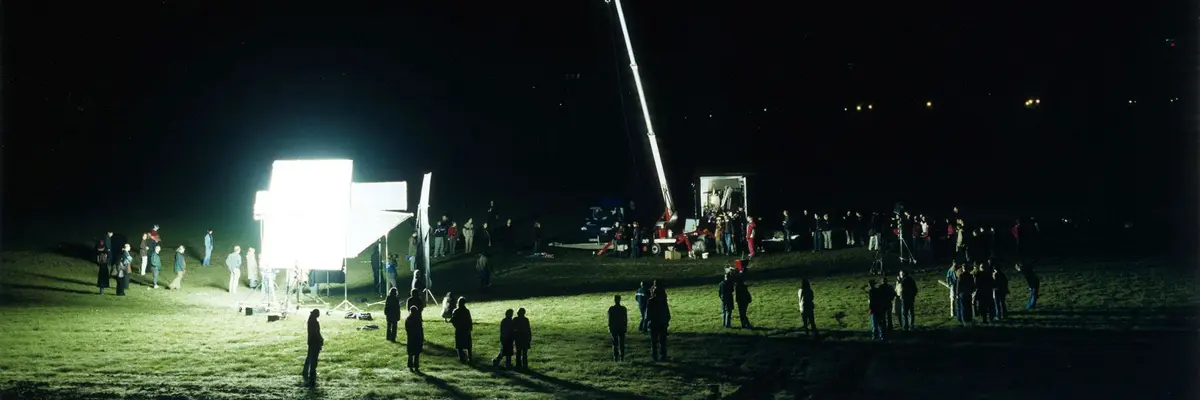 Menschen auf einer Wiese bei Nacht, schauen auf hell leuchtende Leinwand