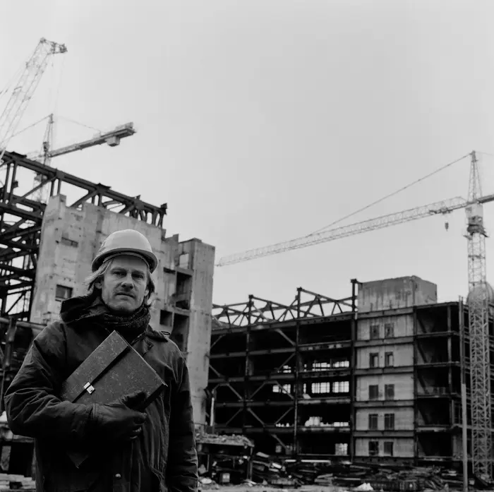 schwarz-weiß Fotografie mit Mann mit Bauarbeiterhelm im Vordergrund und Gebäuden und Kränen im Hintergrund