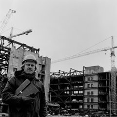 schwarz-weiß Fotografie mit Mann mit Bauarbeiterhelm im Vordergrund und Gebäuden und Kränen im Hintergrund
